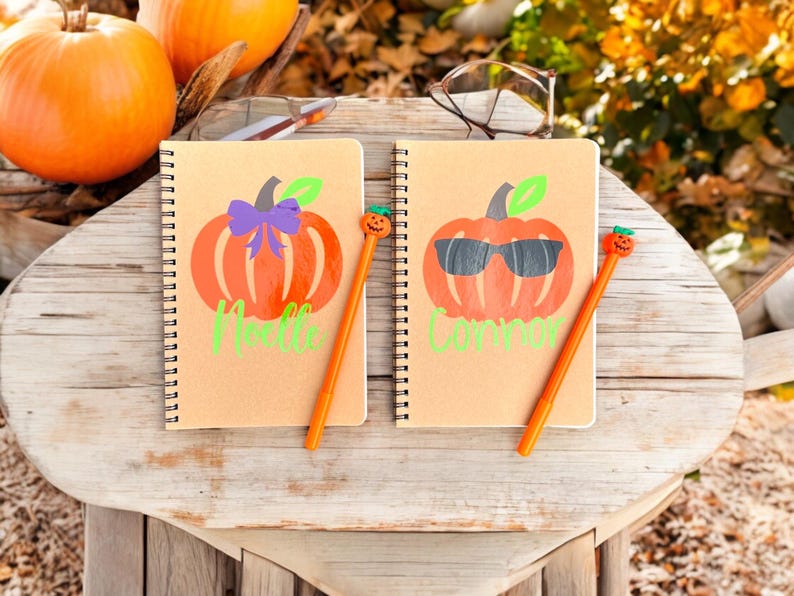 May include: Two brown spiral notebooks with pumpkin designs and names "Melle" and "Connor" written on them. Each notebook has a pumpkin-shaped pen with a smiling face.