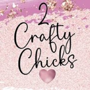 May include: A pink and gold background with the text "2 Crafty Chicks" in black lettering. A pink heart is below the text.