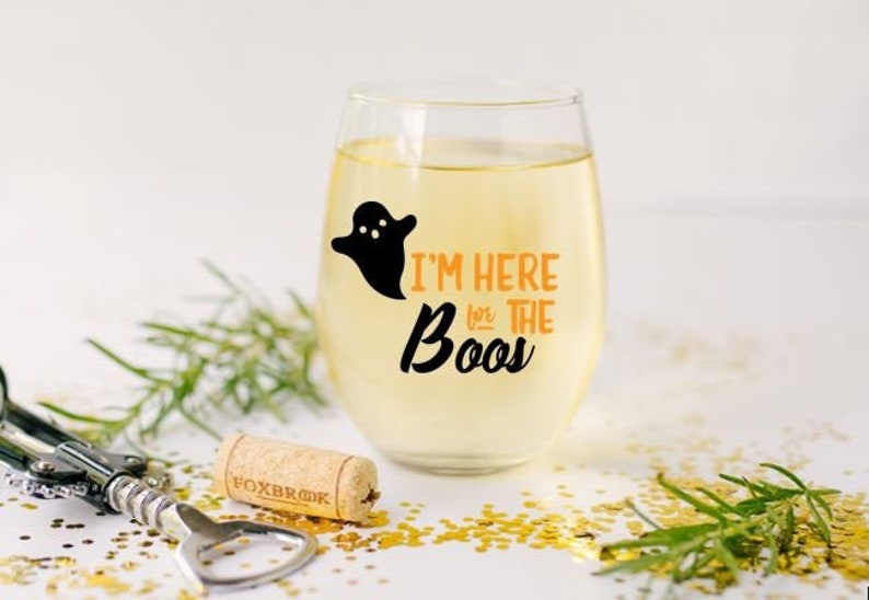 May include: A clear glass wine glass with a black ghost and orange text that reads "I'm here for the boos".