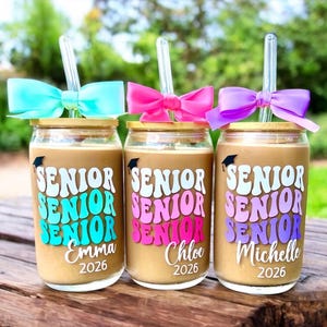 May include: Three glass tumblers with bamboo lids and clear glass straws, each topped with a colorful bow. The glasses feature the word SENIOR in stacked, wavy lettering, a small graduation cap icon, and the names Emma, Chloe, and Michelle with 2026.