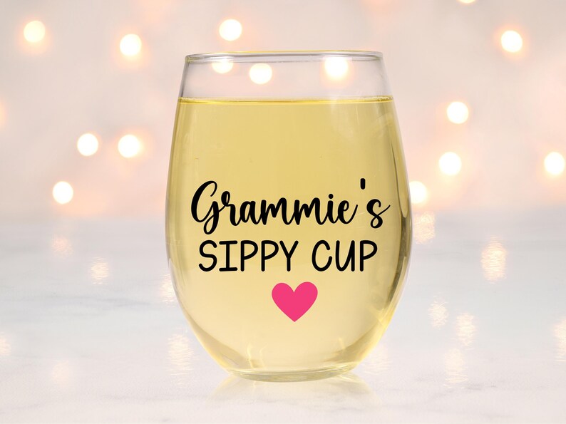 May include: A clear glass wine glass with a pink heart and the text "Gramie's Sippy Cup" in black lettering.