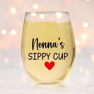 May include: A clear glass wine glass with the text "Nonna's Sippy Cup" and a red heart printed on the front.