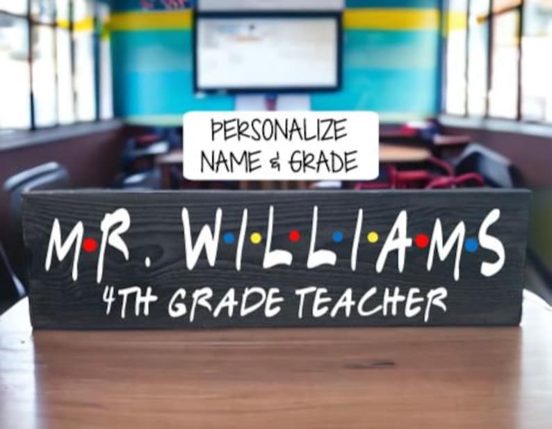 May include: Black wooden sign with white text that reads "Mr. Williams 4th Grade Teacher" in a "Friends" inspired font. The sign has colorful dots between the letters.