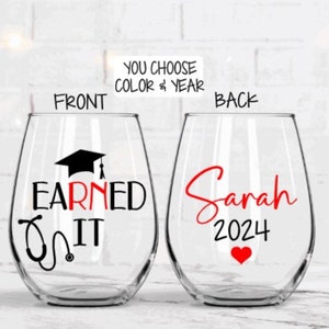 May include: Two stemless wine glasses with a graduation theme. The front glass has a black graduation cap and stethoscope with the text "Earned It". The back glass has the name "Sarah" and the year "2024" in red.