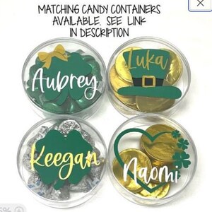 May include: Four clear plastic containers filled with gold coins and green shamrock-shaped candies. Each container has a personalized name label: Aubrey, Keegan, Luka, and Naomi.