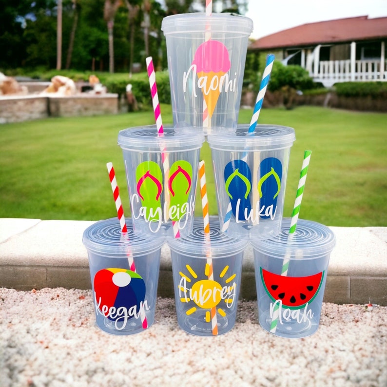 Pu&ograve; includere: Sei bicchieri di plastica trasparente con cannucce colorate e disegni personalizzati. I disegni includono un'anguria, una palla da spiaggia, un sole, infradito e un cono gelato. I bicchieri sono impilati uno sopra l'altro.