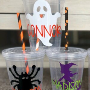 May include: Three clear plastic cups with Halloween-themed designs and names. The top cup has a white ghost with a red smile and the name "CONNOR". The middle cup has a black spider with red eyes and the name "JACKSON". The bottom cup has a purple witch with a black hat and the name "MADISON".