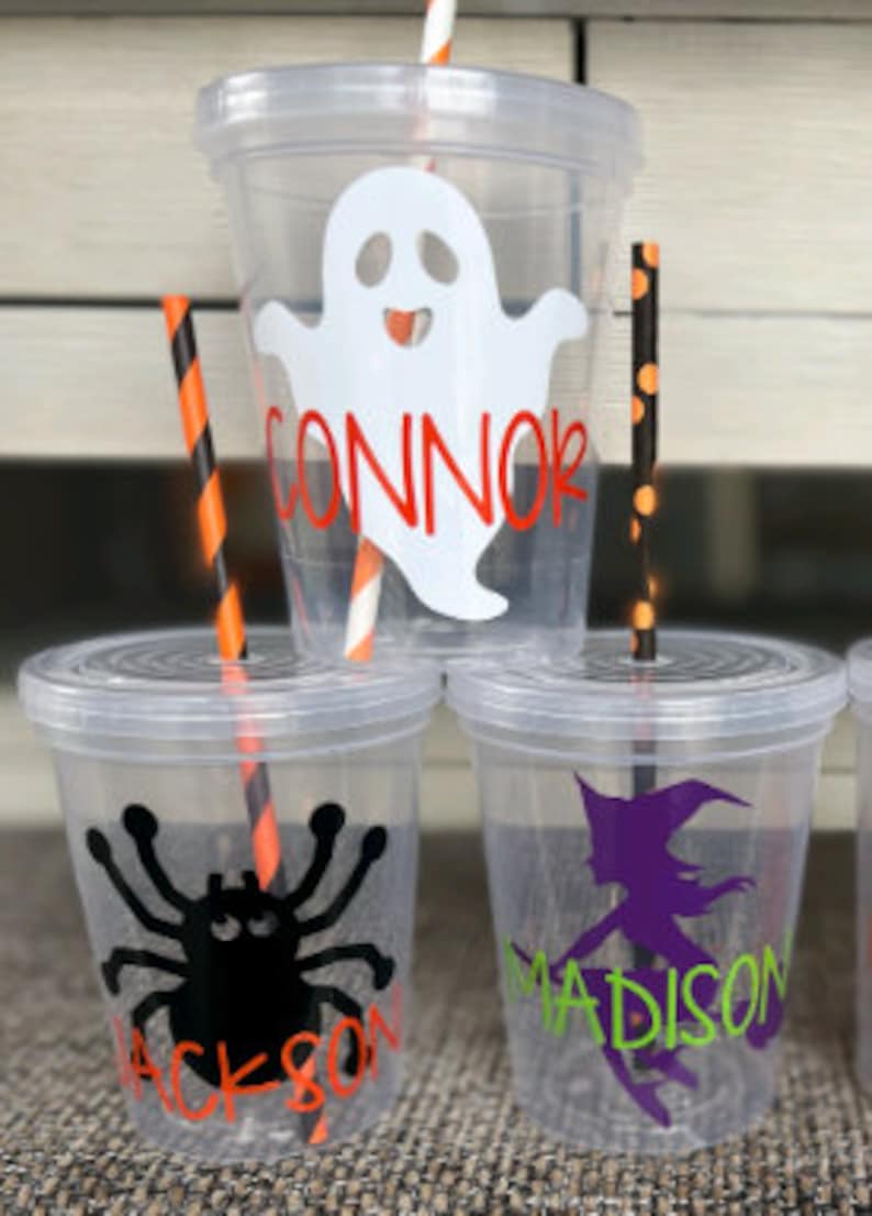 May include: Three clear plastic cups with Halloween-themed designs and names. The top cup has a white ghost with a red smile and the name "CONNOR". The middle cup has a black spider with red eyes and the name "JACKSON". The bottom cup has a purple witch with a black hat and the name "MADISON".