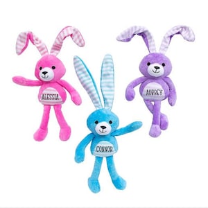 May include: Three plush bunny toys with long ears and long legs. The bunnies are pink, purple, and blue. Each bunny has a name tag on its chest. The pink bunny's tag says "Alessia", the purple bunny's tag says "Aubrey", and the blue bunny's tag says "Connor".