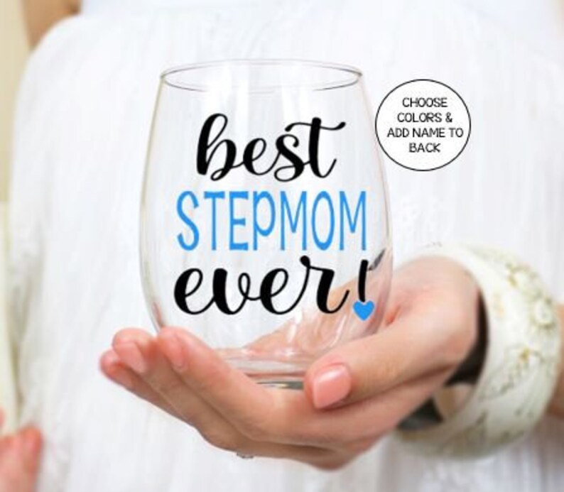 May include: A clear glass wine glass with the text "best stepmom ever!" in black lettering with a blue heart. The word "stepmom" is in blue lettering.