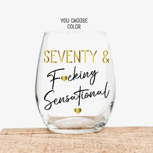 May include: A clear glass wine glass with the text "SEVENTY & F*cking Sensational" in gold lettering. The text is in a handwritten font.