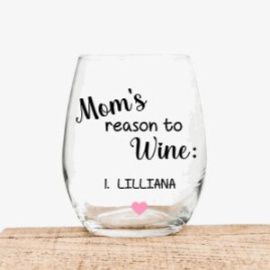 May include: A clear glass wine glass with the text "Mom's reason to wine: 1. Lilliana" in black lettering. A pink heart is below the text.
