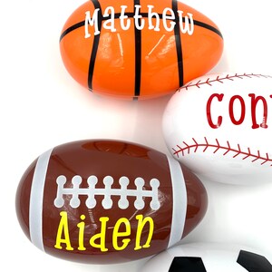 May include: Four plastic Easter eggs decorated with different sports themes. The eggs are white, orange, brown, and white with black accents. The names Matthew, Aiden, and Connor are written on the eggs.
