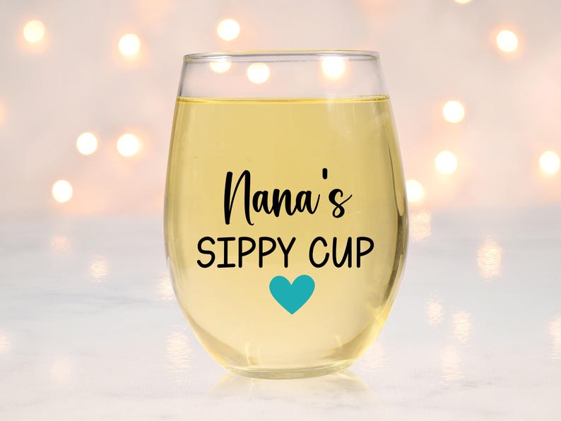 May include: A clear glass wine glass with the text "Nana's Sippy Cup" and a blue heart on the front.