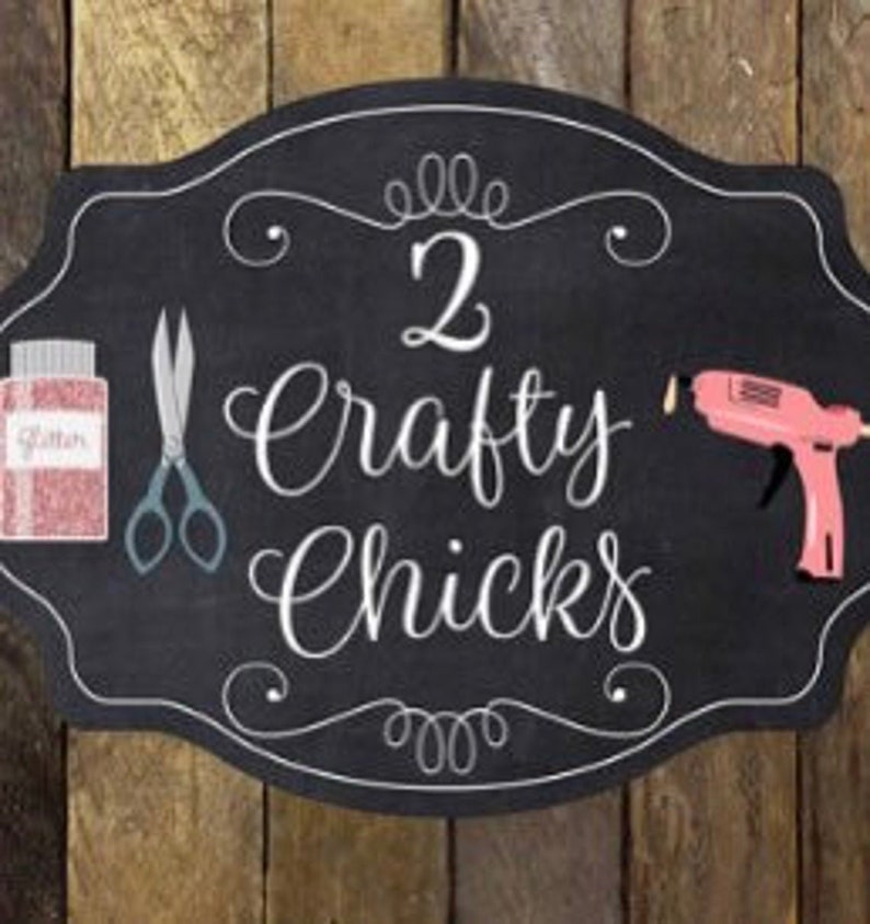 May include: Black chalkboard sign with white lettering that reads "2 Crafty Chicks". The sign has a decorative border and includes images of scissors, glitter, and a glue gun.
