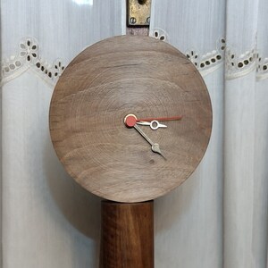 May include: A wooden clock with a round face and a dark brown finish. The clock has a red second hand and a silver hour and minute hand. The clock is standing on a wooden base.