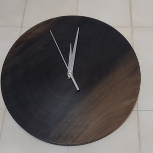 May include: A round, dark wood clock with silver hands. The clock face is a gradient of dark brown to black.