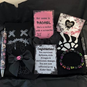 May include: A black gift box containing emo-themed items. It features a black sweater with a skull design, a pen with skull detailing, a bracelet, a scrunchie, a choker, and cards with the text "Her name is Rachel" and "Congratulations!"