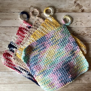 May include: Four handmade crochet washcloths in various colors. One is red, white, and navy striped, another is yellow and beige, and the third is pastel rainbow. Each has a matching loop for hanging.