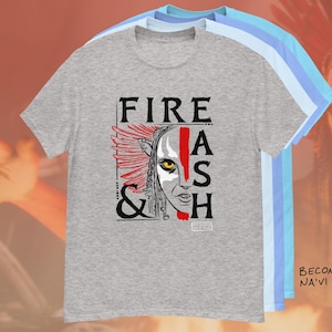 Pode incluir: Uma camiseta cinza com o texto "FIRE & ASH" em preto, com um gráfico de um rosto com detalhes em vermelho e amarelo. A camiseta faz parte de uma pilha de outras camisetas em azul claro e azul.