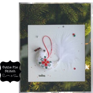 May include: White felt bird ornament with red and green embroidered flower design and white feather tail. The ornament is hanging from a red string.