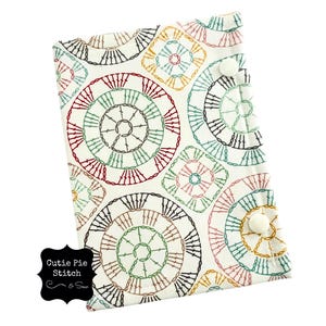 May include: White fabric with a repeating pattern of colorful crocheted circles and squares. The fabric has a label that says "Cutie Pie Stitch & Sew".