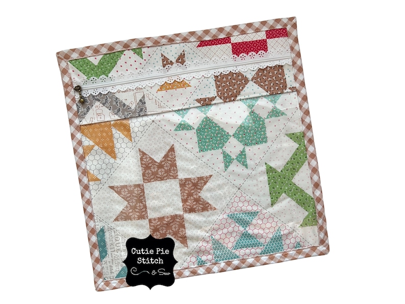 May include: A quilted zippered pouch with a patchwork design in shades of brown, green, and orange. The pouch features a white lace trim and a brown and white gingham border. The text "Cutie Pie Stitch & Sew" is visible.