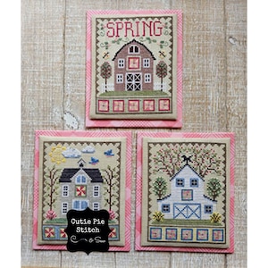 Peut inclure: Trois broderies au point de croix représentant une ferme avec un extérieur rouge, gris et blanc. Les motifs sont encadrés d'une bordure vichy rose et blanche. Le motif du haut indique "SPRING". Le motif en bas à gauche comprend le texte "Cutie Pie Stitch & Sew".