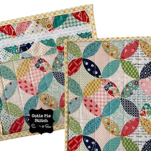 May include: A quilted fabric pouch with a zipper closure and a white lace trim. The pouch is decorated with a patchwork design of colorful circles and the text "Cutie Pie Stitch".