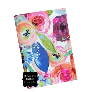 May include: A floral print case with a white background, featuring pink, orange, and purple flowers, and blue leaf accents. The case has a pink button closure and the text "Cutie Pie Stitch & Sew".
