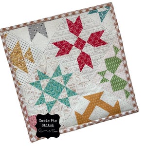 May include: A square, quilted patchwork featuring various geometric shapes in red, teal, gold, and green on a white background. The quilt has a brown and white checkered border and the text "Cutie Pie Stitch & Sew".