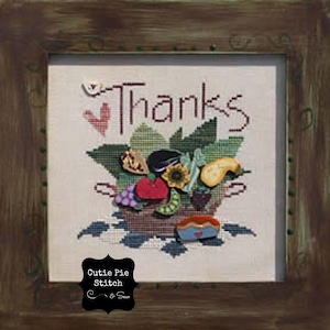 May include: A framed cross-stitch design with the word "Thanks" in red lettering. The design features a basket overflowing with colorful fruits and vegetables, including a red heart, a sunflower, and a pie. The frame is brown wood with a distressed finish.