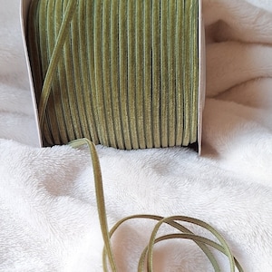 May include: A spool of olive green velvet ribbon. The ribbon is wound around a cardboard spool and is ready to be used for crafting or decorating.