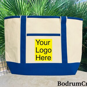 May include: A large, white canvas tote bag with blue trim and handles. The bag has a yellow pocket with the text "Your Logo Here" printed on it.