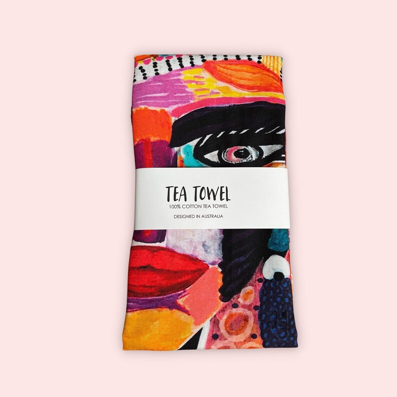 Pu&ograve; includere: Un asciugamano da t&egrave; colorato con un design di viso astratto. L'asciugamano &egrave; in 100% cotone e progettato in Australia. Il testo "TEA TOWEL 100% COTTON TEA TOWEL DESIGNED IN AUSTRALIA" &egrave; stampato su un'etichetta bianca.
