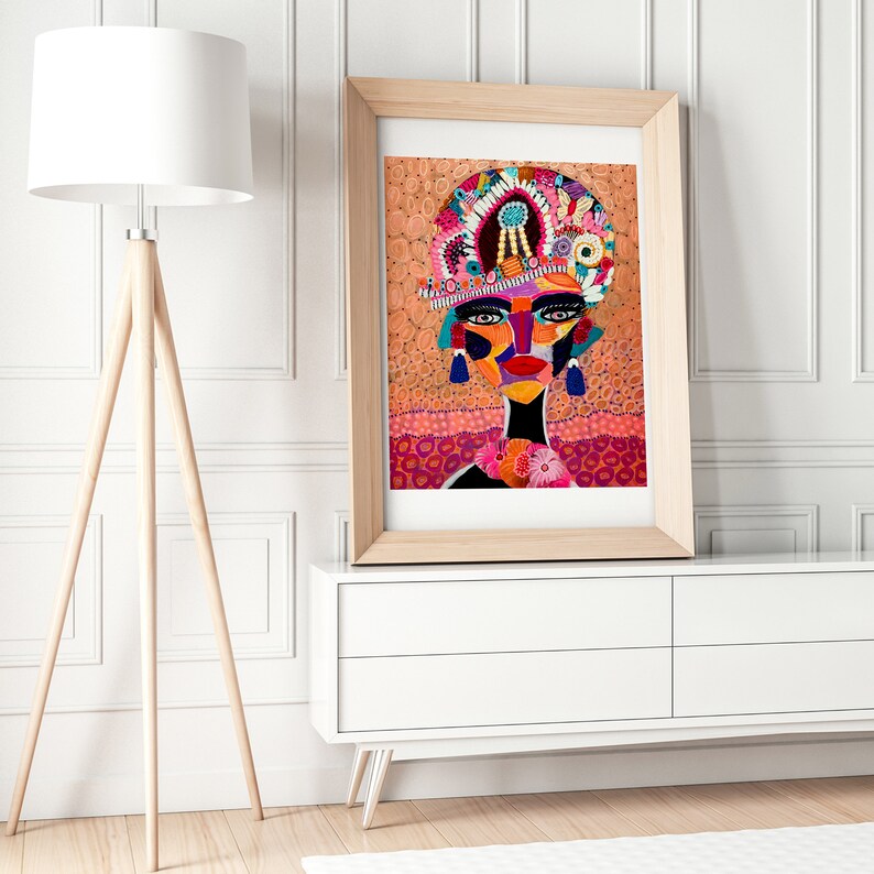 Pu&ograve; includere: Una stampa incorniciata di un ritratto astratto colorato di una donna con un grande copricapo ornato. Lo sfondo &egrave; di un arancione vibrante con motivi floreali rosa e bianchi.
