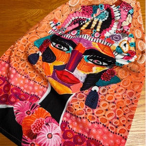 Pu&ograve; includere: Un tessuto colorato con un grande disegno di viso astratto. Il viso &egrave; dipinto con colori vivaci, tra cui rosa, arancione, giallo, blu e verde. Il tessuto &egrave; decorato con piccoli punti bianchi e un motivo floreale.