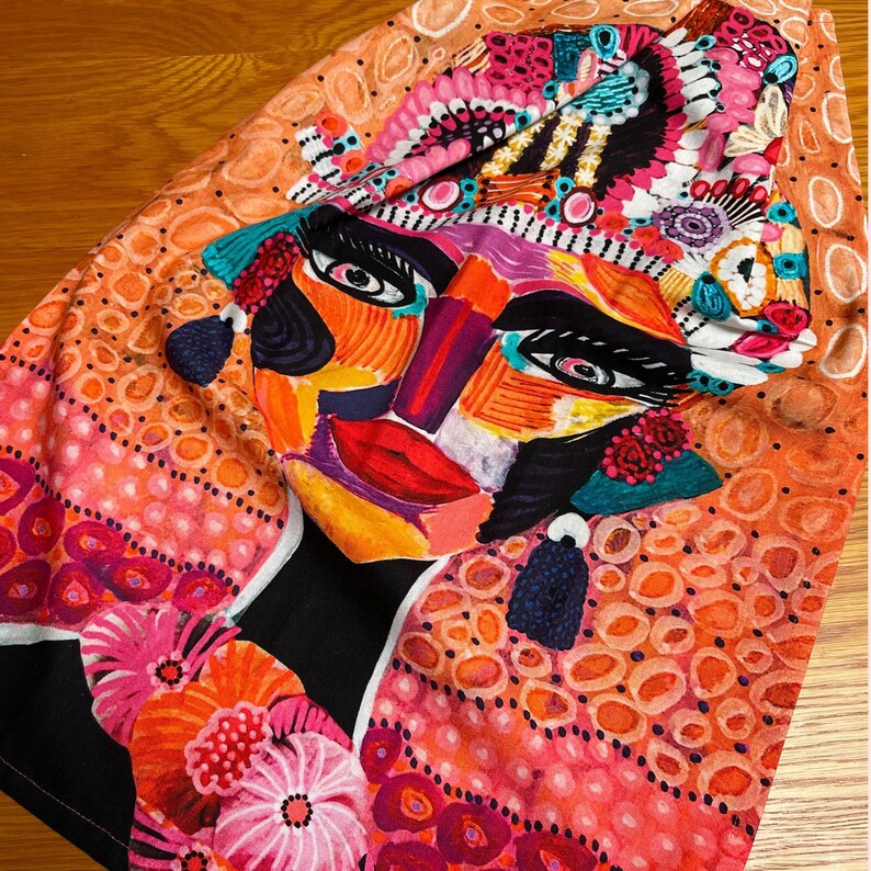 Pu&ograve; includere: Un tessuto colorato con un grande disegno di viso astratto. Il viso &egrave; dipinto con colori vivaci, tra cui rosa, arancione, giallo, blu e verde. Il tessuto &egrave; decorato con piccoli punti bianchi e un motivo floreale.