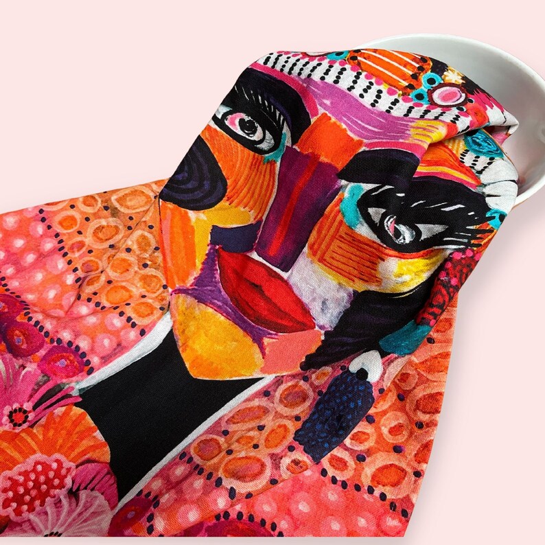 Pu&ograve; includere: Un viso astratto colorato stampato su un tessuto rosa e arancione con sfondo nero. Il tessuto ha un motivo a pois.