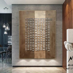 May include: A modern abstract art piece with a geometric pattern of small squares in a light brown frame. The artwork is hanging on a gray wall in a contemporary interior design setting.