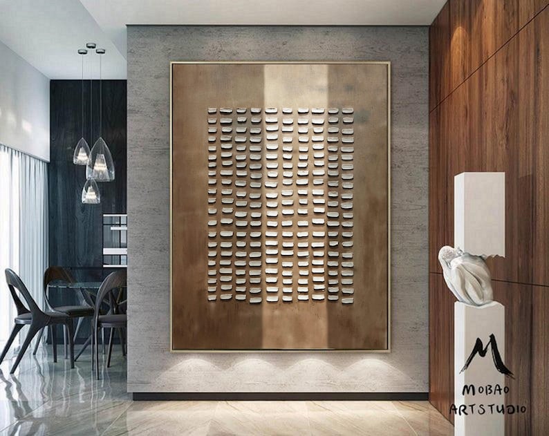 May include: A modern abstract art piece with a geometric pattern of small squares in a light brown frame. The artwork is hanging on a gray wall in a contemporary interior design setting.