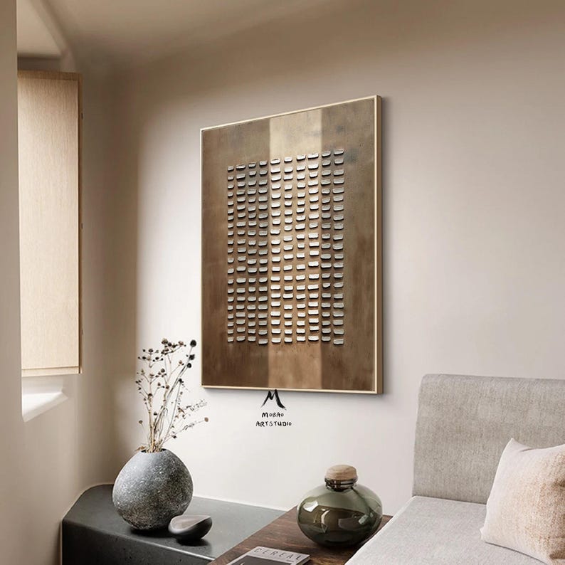 May include: A modern abstract wall art piece with a geometric pattern of small squares in shades of brown and white. The artwork is framed in a light brown wood frame and hangs on a white wall.