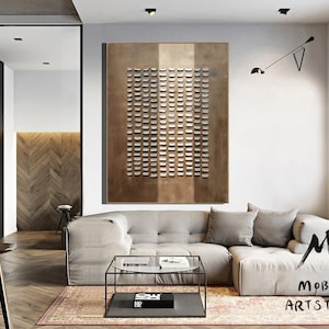 May include: A modern living room with a large, abstract metal wall art piece featuring a geometric pattern of squares. The art is in shades of brown and white. A large, light gray sectional sofa with a glass coffee table sits in front of the art. The room has hardwood floors and a large window.