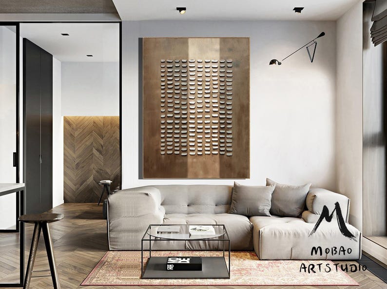 May include: A modern living room with a large, abstract metal wall art piece featuring a geometric pattern of squares. The art is in shades of brown and white. A large, light gray sectional sofa with a glass coffee table sits in front of the art. The room has hardwood floors and a large window.