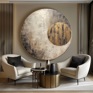 Peut inclure: Une grande œuvre d'art murale circulaire présentant un design abstrait texturé dans des tons crème, gris et noir avec un cercle doré superposé. Deux fauteuils crème avec des coussins noirs entourent une table d'appoint et une table basse dorée.