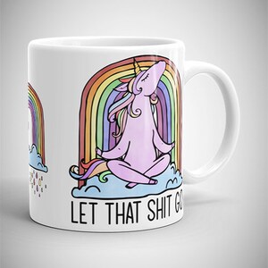 May include: White ceramic mug featuring a cartoon unicorn meditating in front of a rainbow. The unicorn is pink with a yellow horn and colorful mane. The text "LET THAT SHIT GO" is printed below the unicorn.