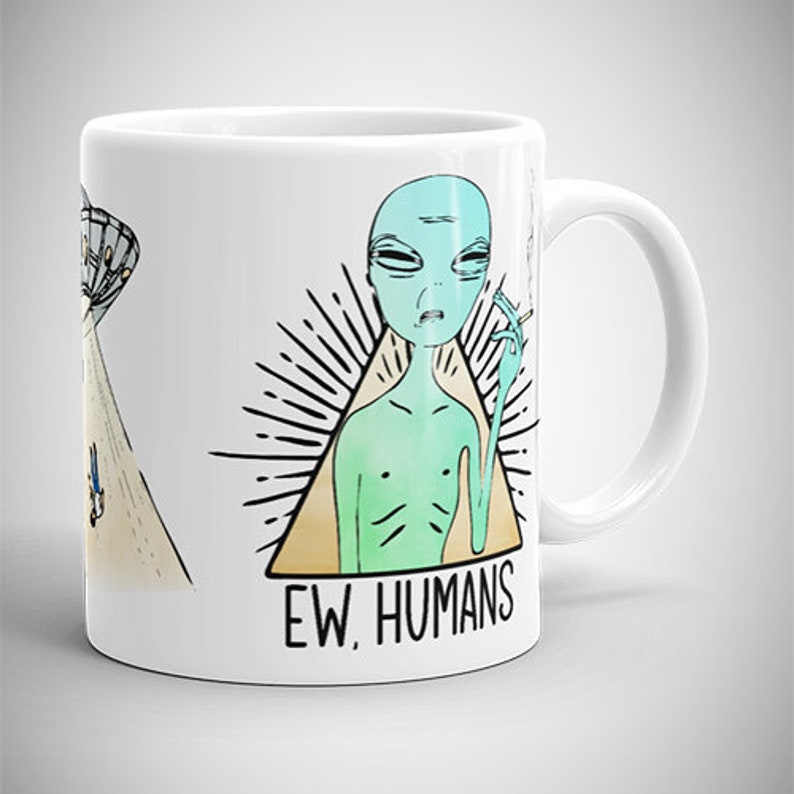 May include: White ceramic mug with a green alien smoking a cigarette inside a triangle with the text "EW. HUMANS". The alien has a blue head and a green body. There is a UFO in the background.