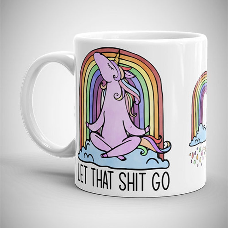 May include: White ceramic mug featuring a meditating unicorn in front of a rainbow. The unicorn is pink with a yellow horn and colorful mane and tail. The text "LET THAT SHIT GO" is printed below the unicorn. A second rainbow is on the right.