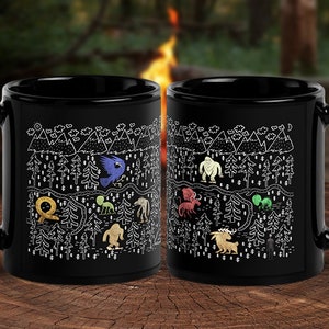 May include: Two black coffee mugs with white illustrations of a forest scene with mythical creatures. The mugs have a white outline of a forest with mountains, trees, and a winding path. The creatures include a sasquatch, a griffin, a dragon, a unicorn, a kraken, and a werewolf.