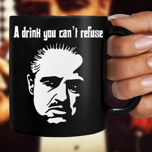 Puede incluir: Taza de café negra con una silueta blanca de un rostro de hombre y el texto "A drink you can't refuse".